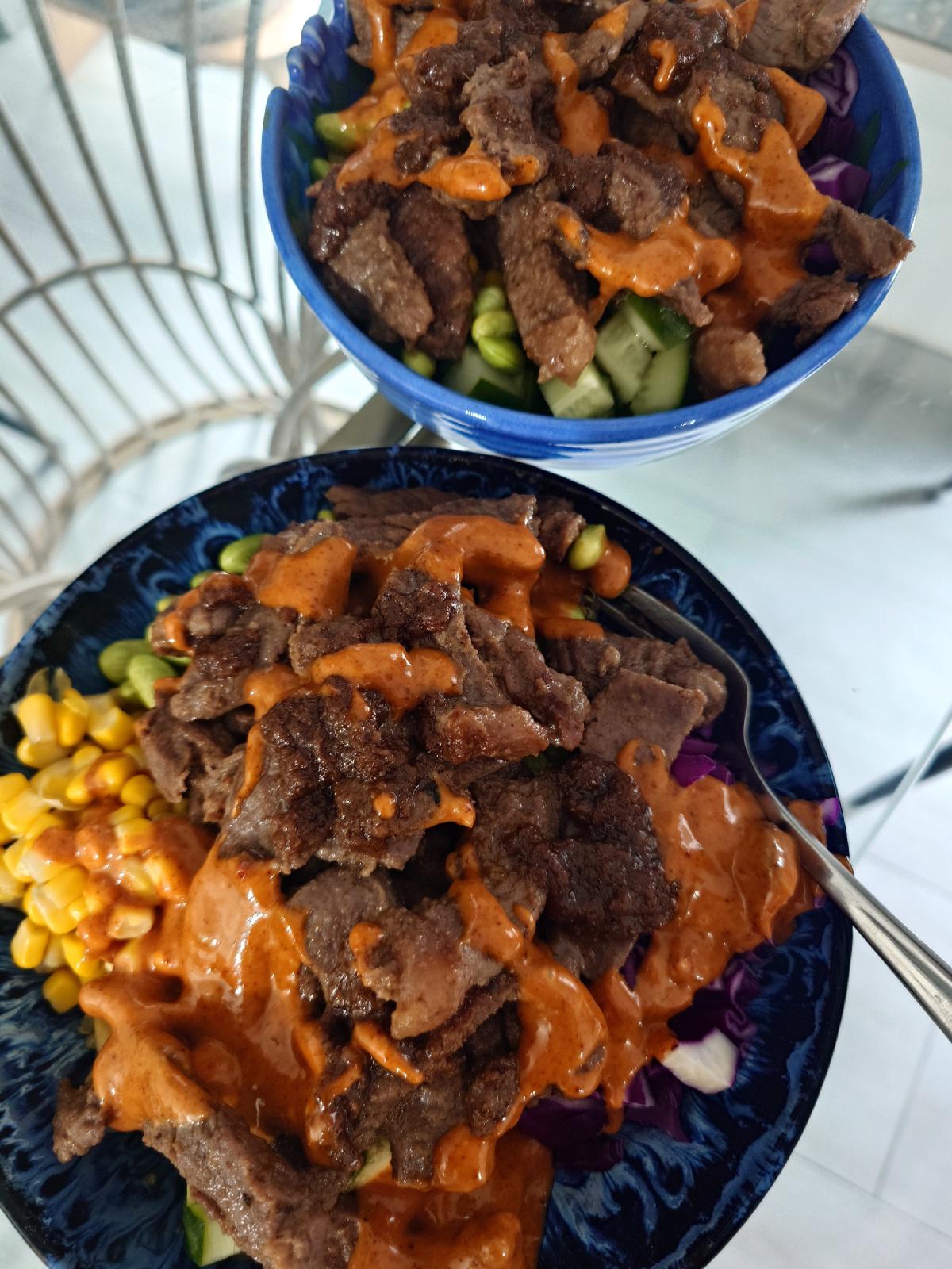 Two finished bowls, beef over quinoa with corn, edamame, cucumber and red cabbage
