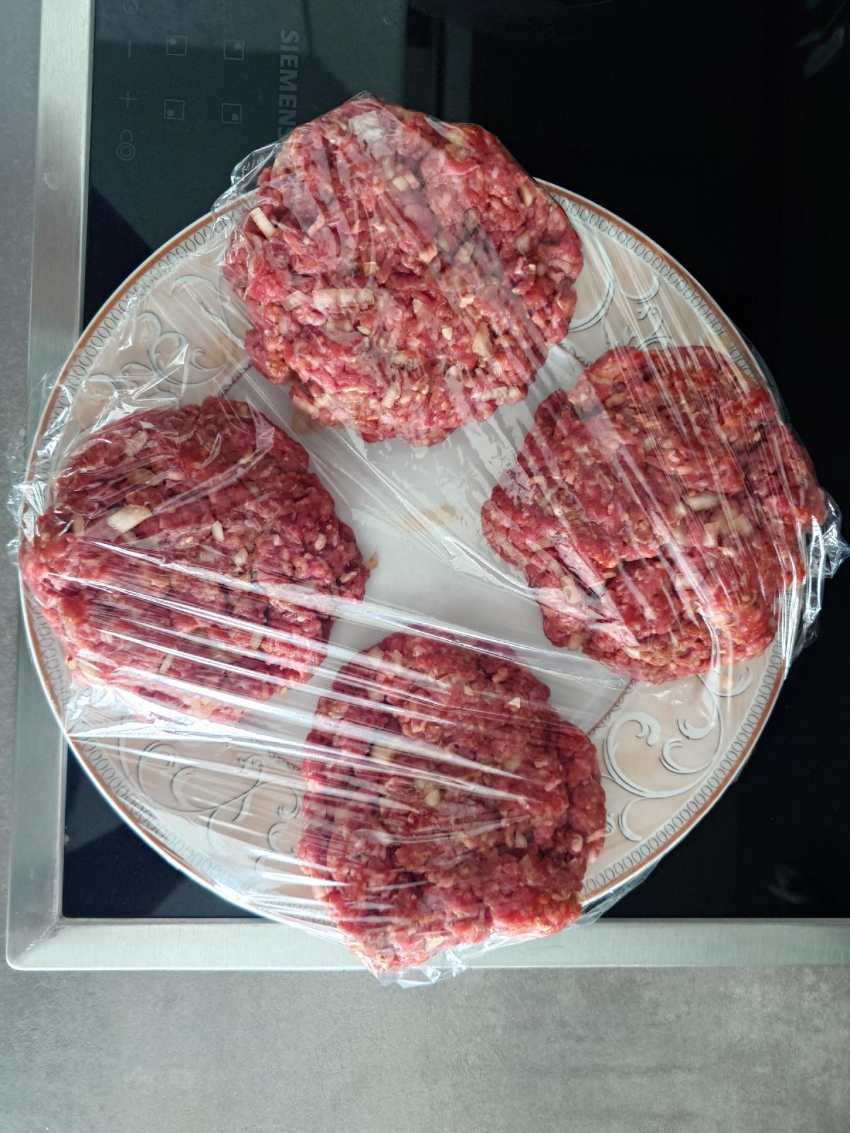 Four formed patties resting under cling film