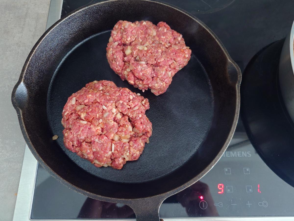 Two raw patties dropped into the smoking-hot cast iron