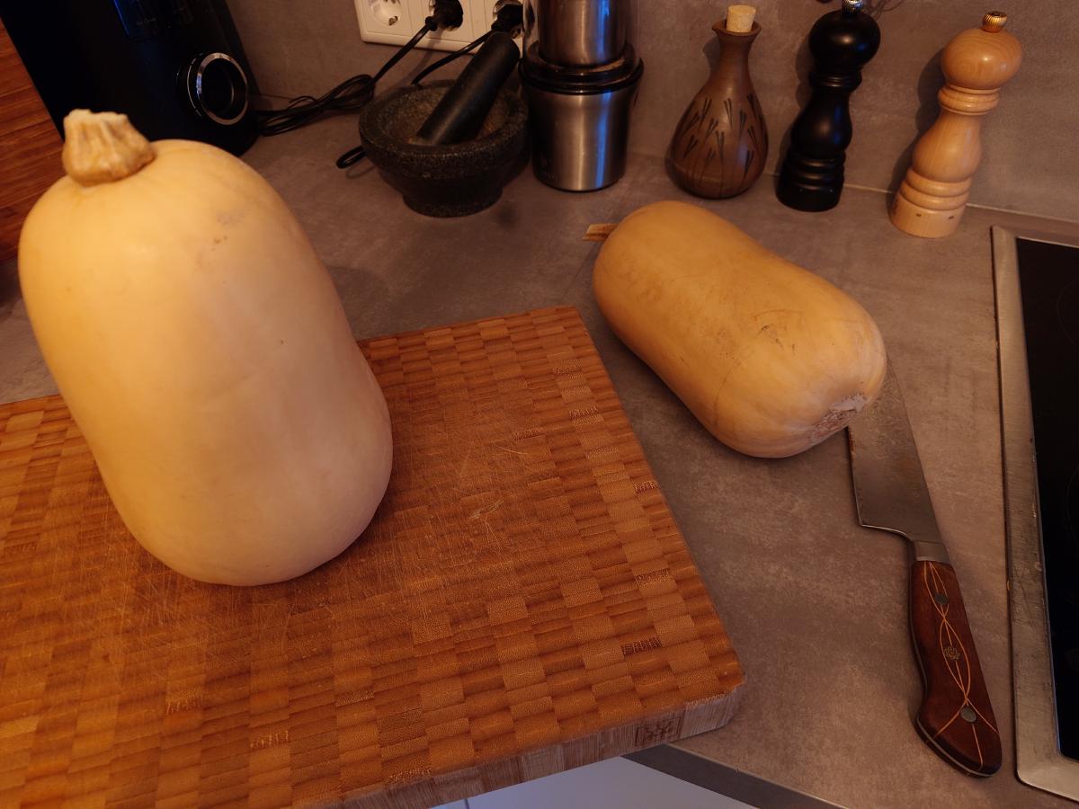 A butternut squash cut into neck and bulb on the counter beside the board and knife