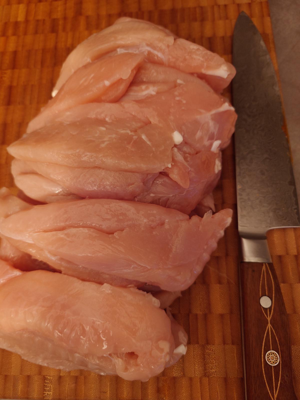 Whole chicken breasts on the board with the knife