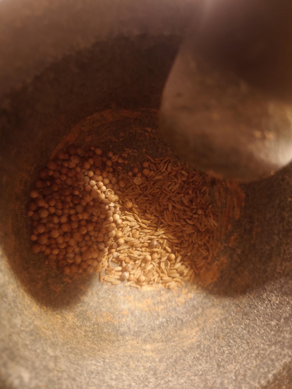 Coriander seed and cumin seed side by side in the mortar