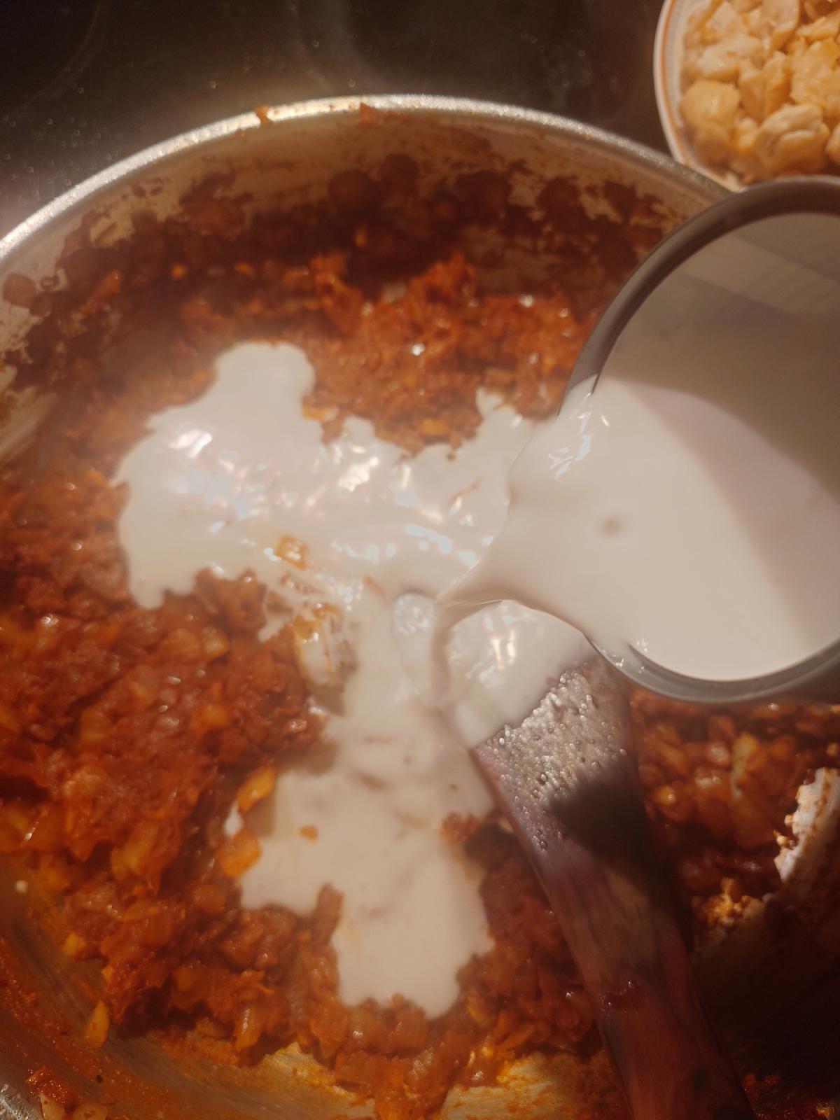 Coconut cream poured from a measuring cup into the spiced onion