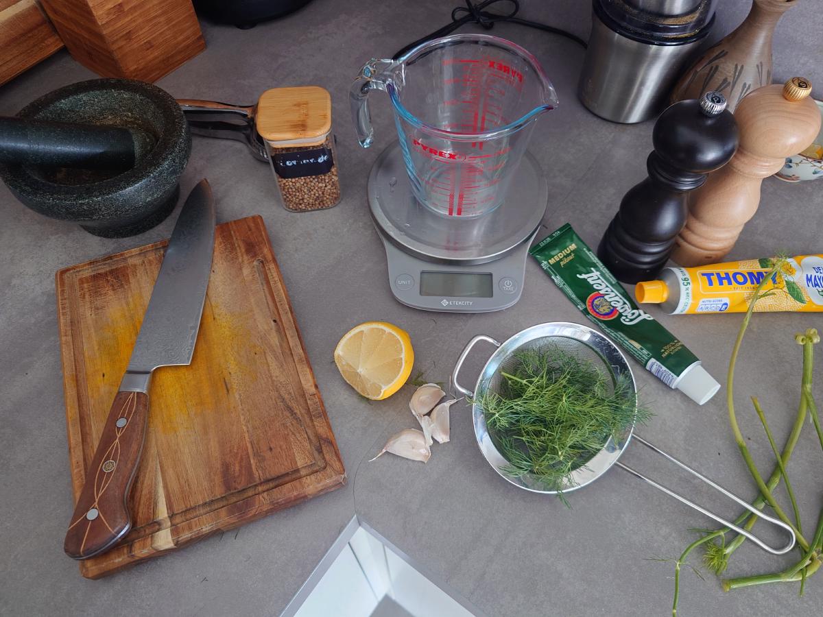 Mortar, garlic, dill, lemon, mustard and mayonnaise laid out on the counter