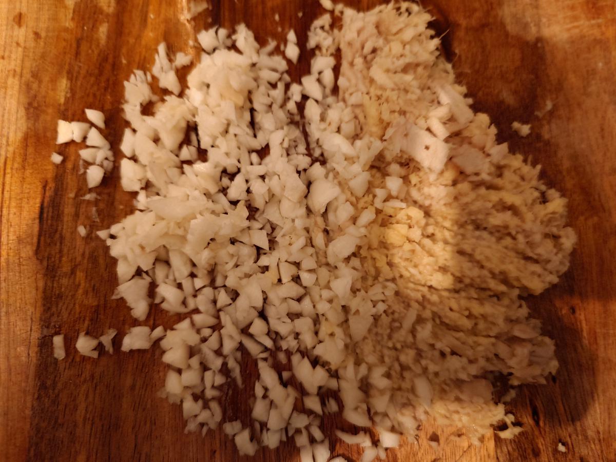 Minced garlic and grated ginger side by side on the board