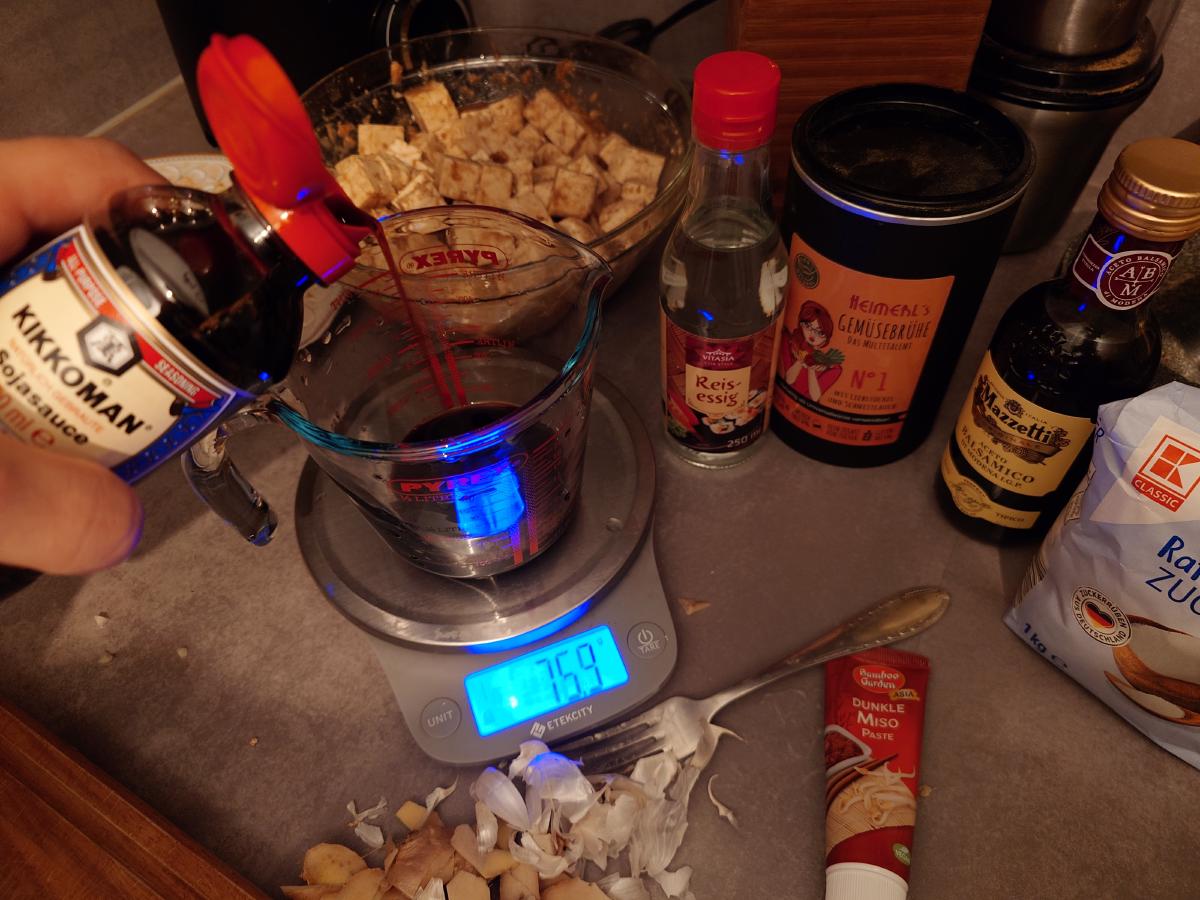 Kikkoman soy sauce poured into a jug on the scale, bottles of rice vinegar, broth, balsamic and sugar lined up behind