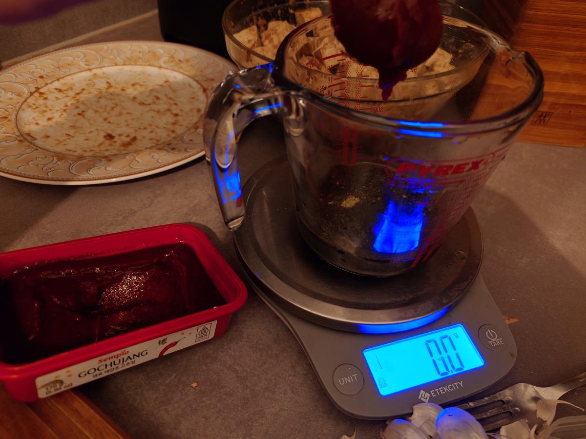 A tub of gochujang held over the jug, the scale tared to zero