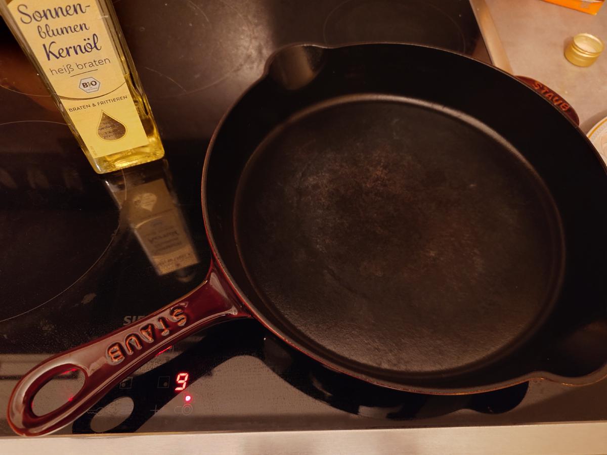 An empty cast iron pan on the induction hob, dial reading 9, a bottle of sunflower oil beside it