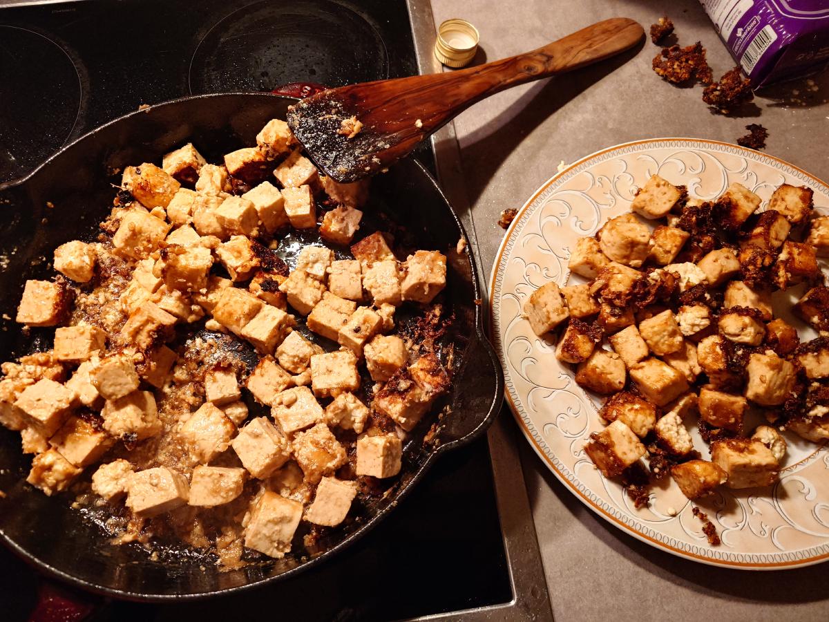 The second batch frying, the first batch on a plate beside it with dark crust fragments scraped off