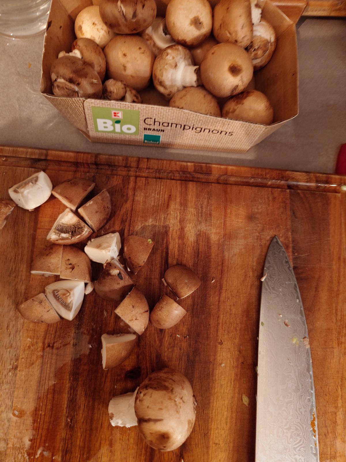 Brown mushrooms quartered on the board, the box behind