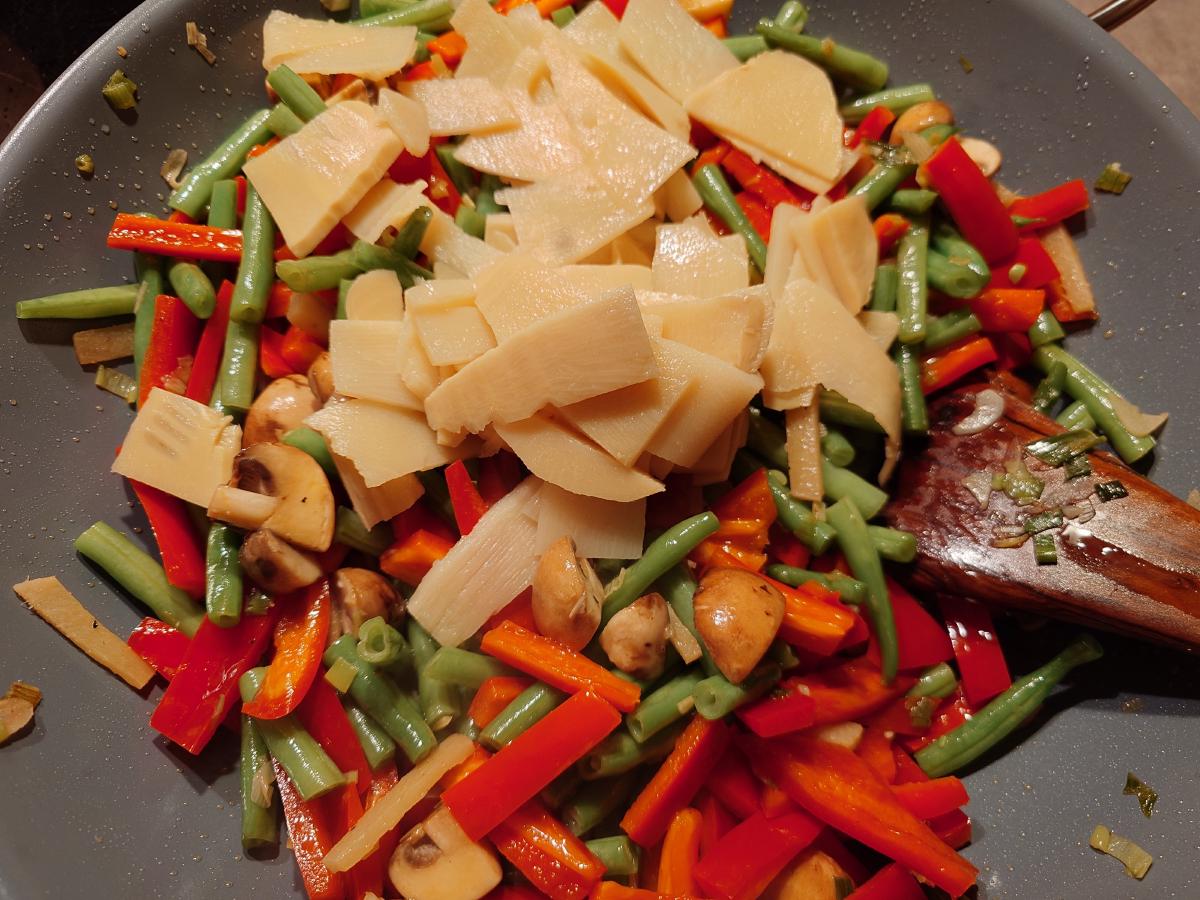 The drained shoots piled on top of the vegetables in the wok