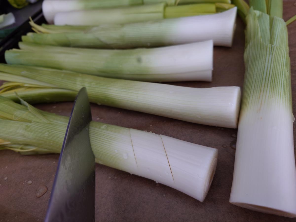 Leeks on the board, one being scored crosswise, the cuts stopping short of the base