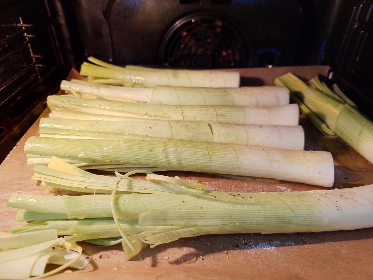 The scored leeks laid out on parchment in the oven, salt and cracked pepper visible on the surface