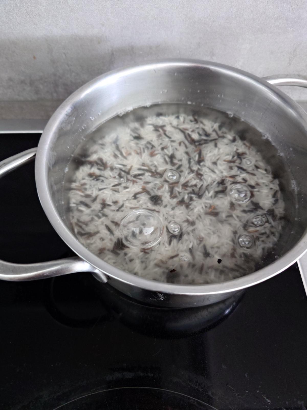 White basmati and dark wild rice grains under water in a steel pot