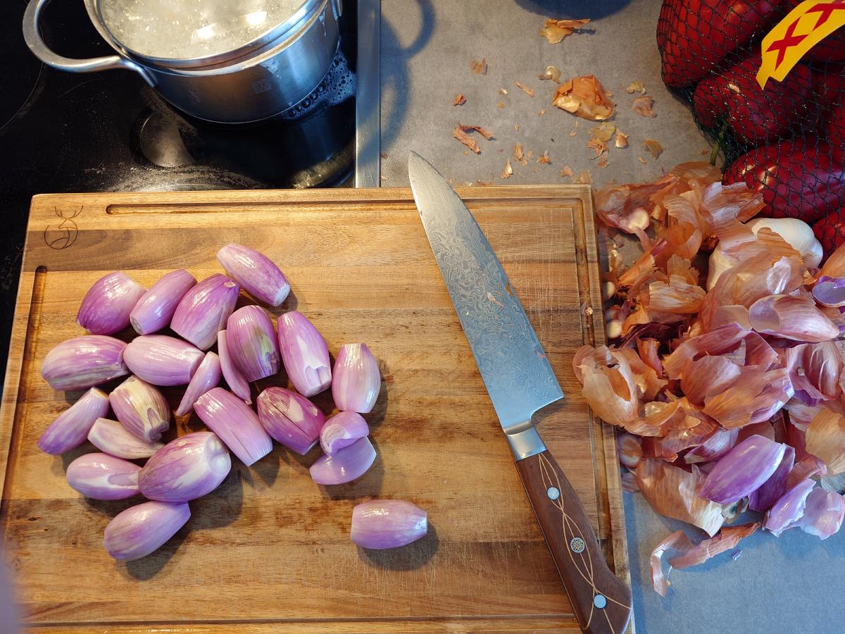 Peeled shallot cloves on the wooden board, skins swept off to the side, the rice pot on the hob behind