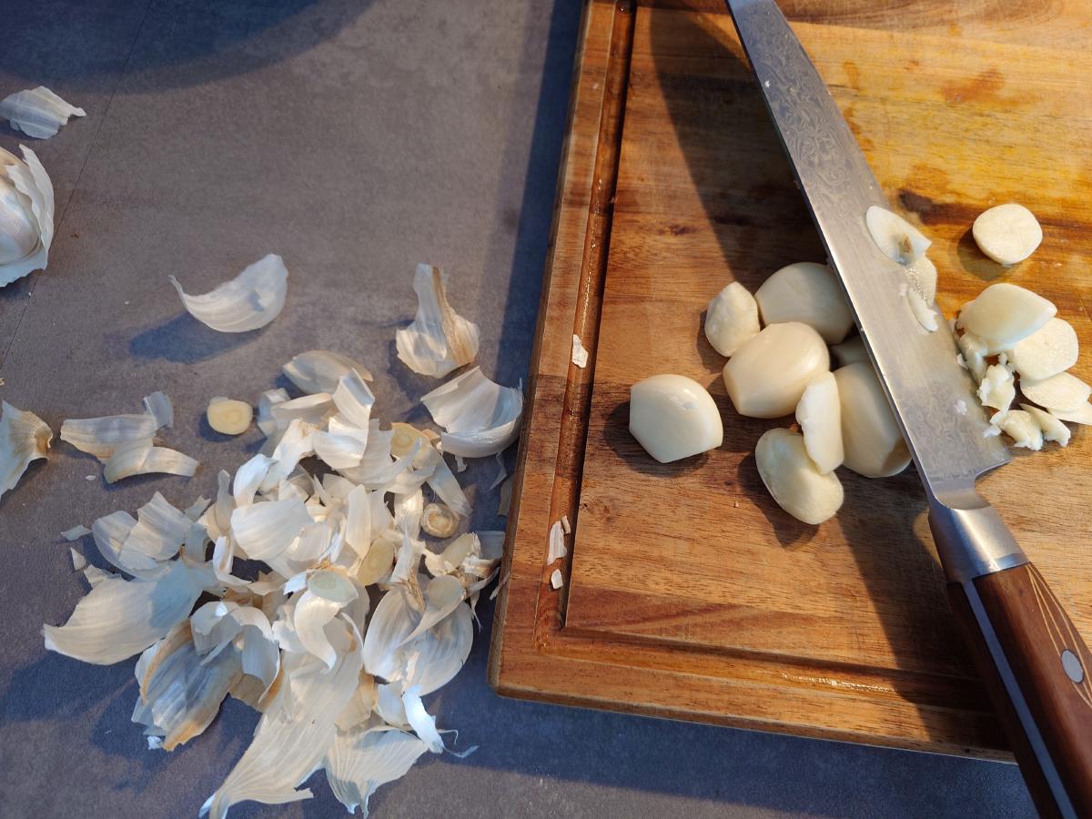 Peeled garlic cloves on the board with the knife, a heap of skins on the counter alongside