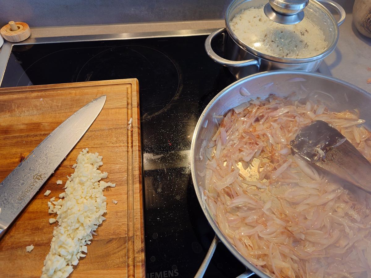 The minced garlic in a line on the board beside the pan of browned shallots