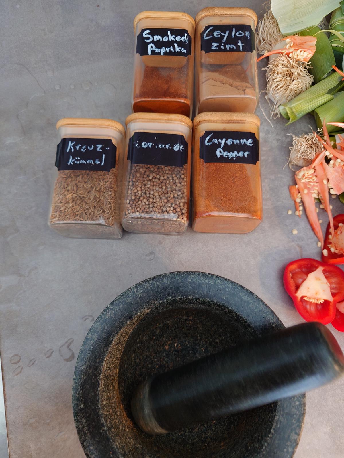 Five labelled spice jars and the granite mortar on the counter, pepper trimmings to the side