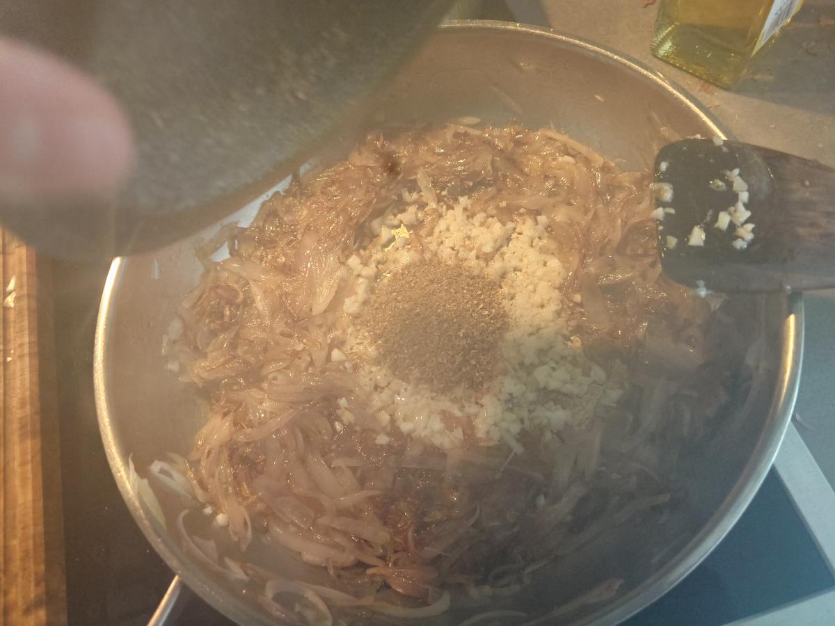 Ground spice tipped from the mortar onto the garlic in the middle of the pan