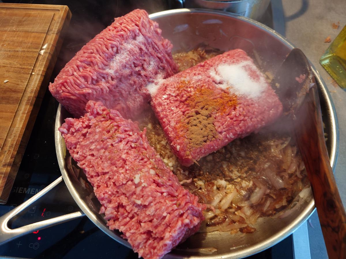 Three blocks of ground beef sitting in the pan on the shallots, salt and red spice on top
