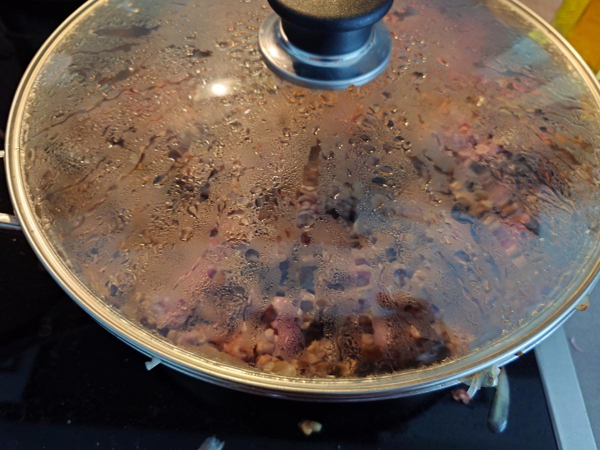 The glass lid on, the pan underneath fogged with condensation