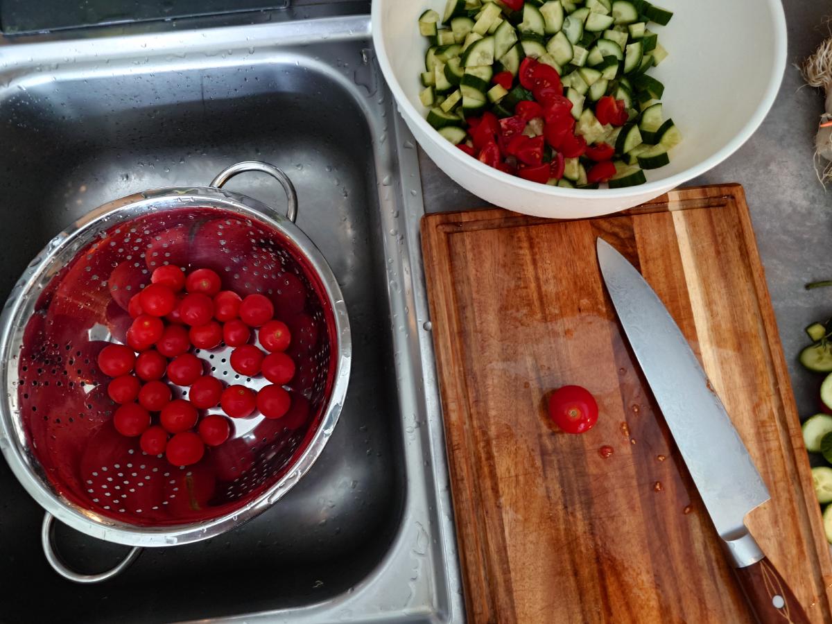 Cherry tomatoes in a colander in the sink, the bowl of cucumber and cut tomato alongside