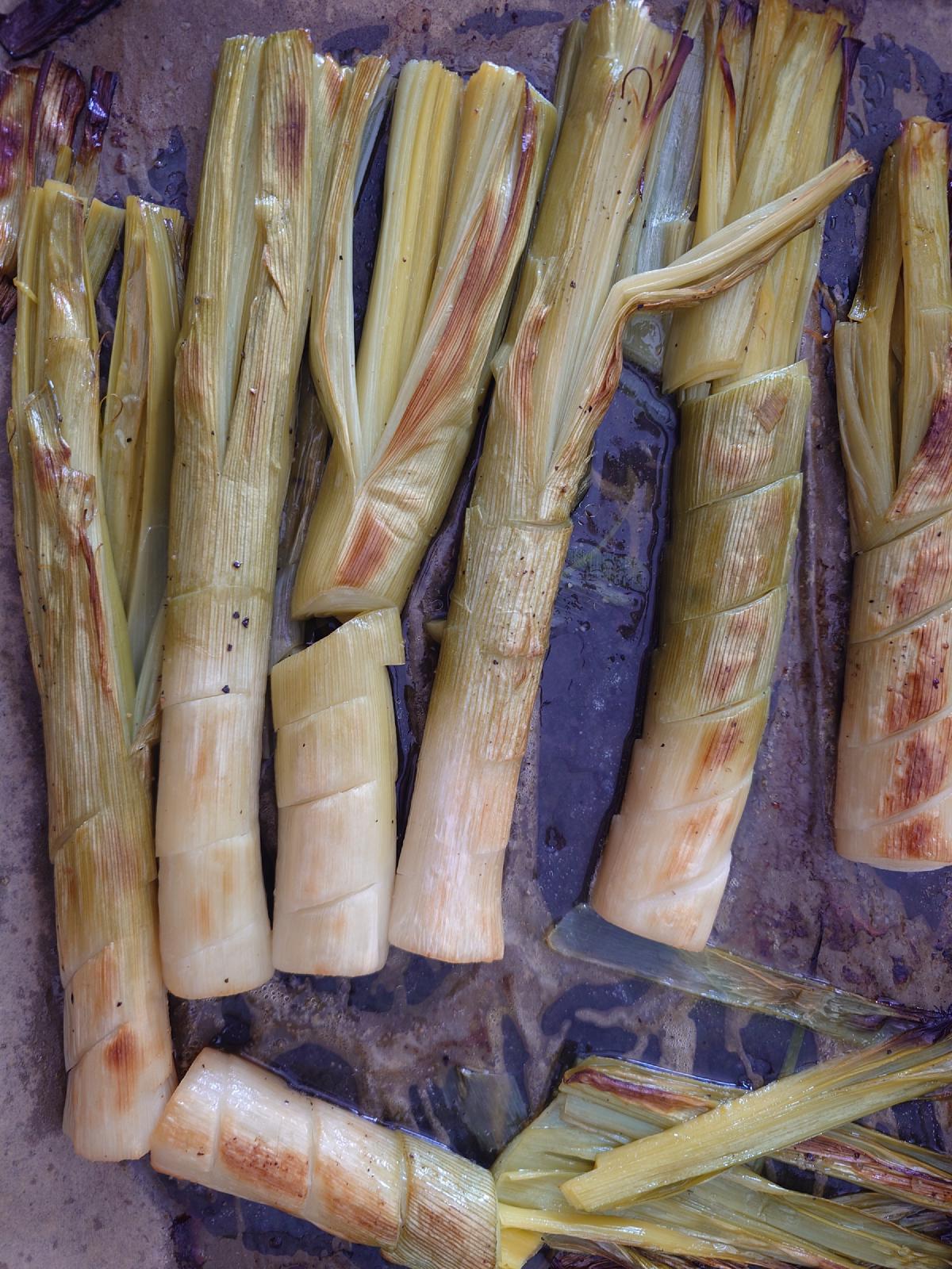 The roasted leeks close up, cut lines browned, the tray dark with their liquid
