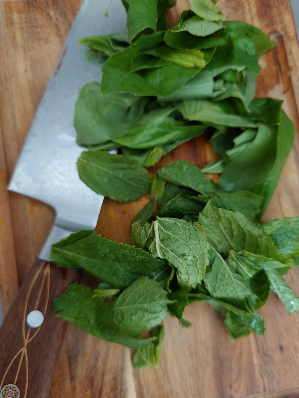 Whole basil and mint leaves heaped on the board under the knife