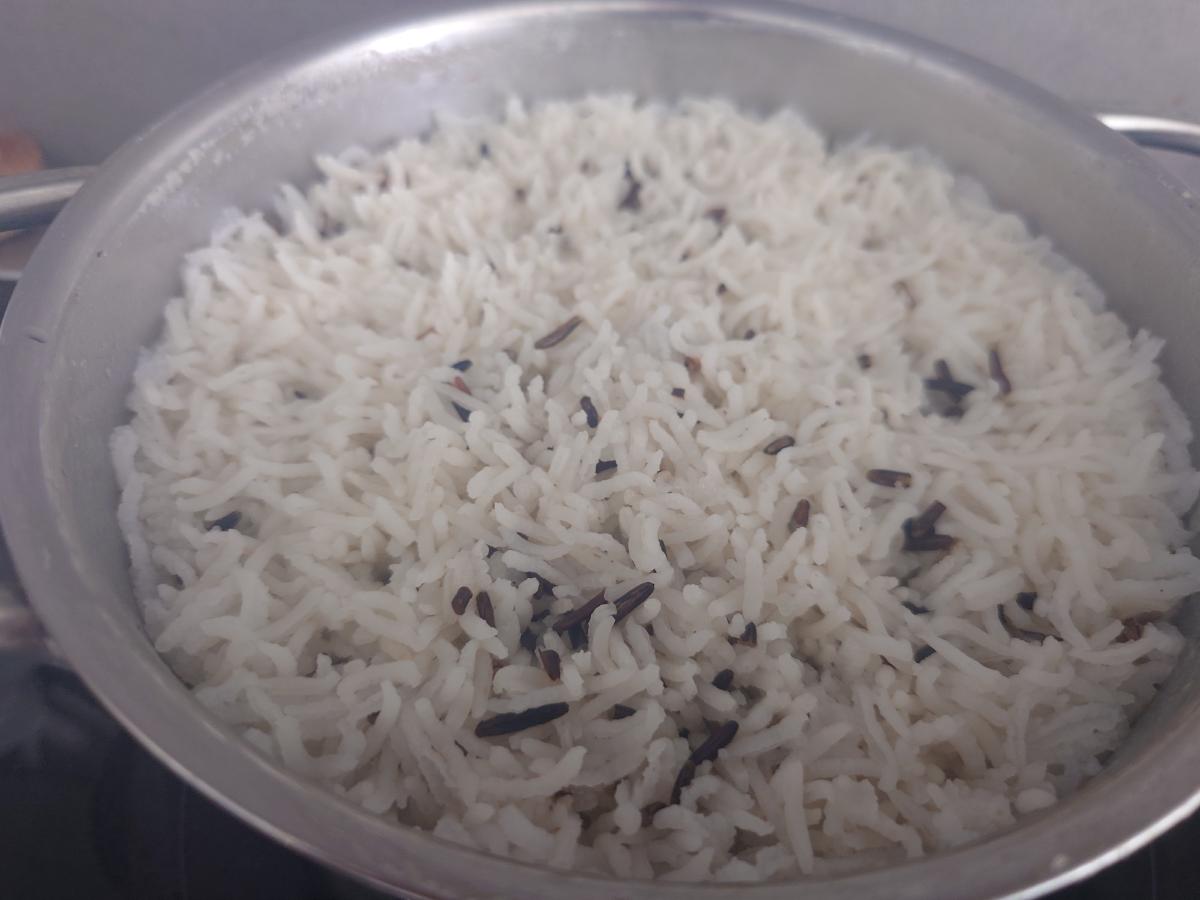 The finished rice in the pot, the surface risen into standing grains, wild rice dark against the white