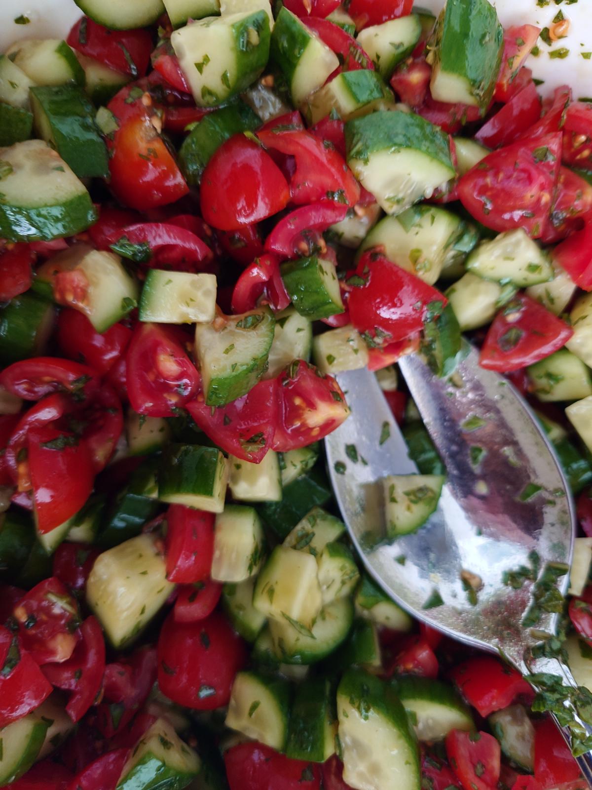 The tossed salad close up, herbs coating every piece of cucumber and tomato