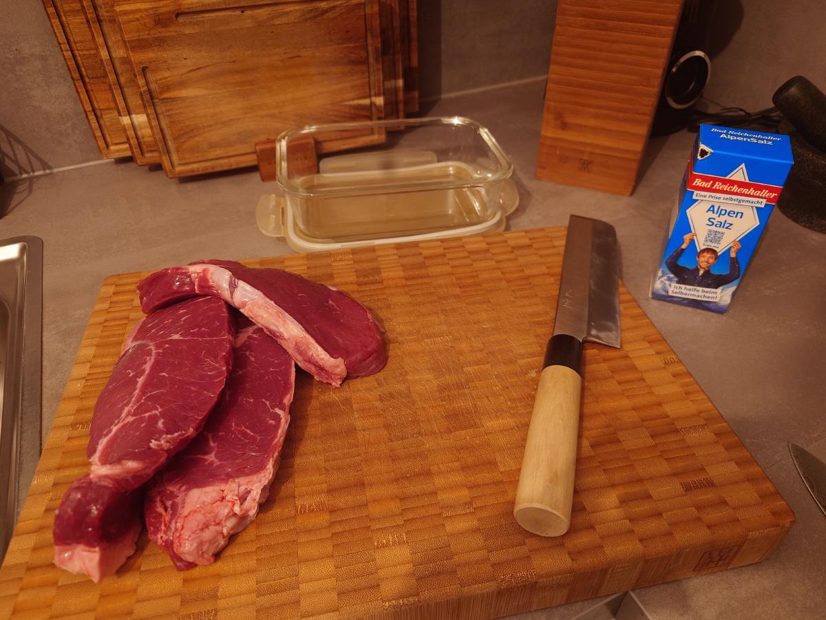 Steaks, salt and the glass container on the board
