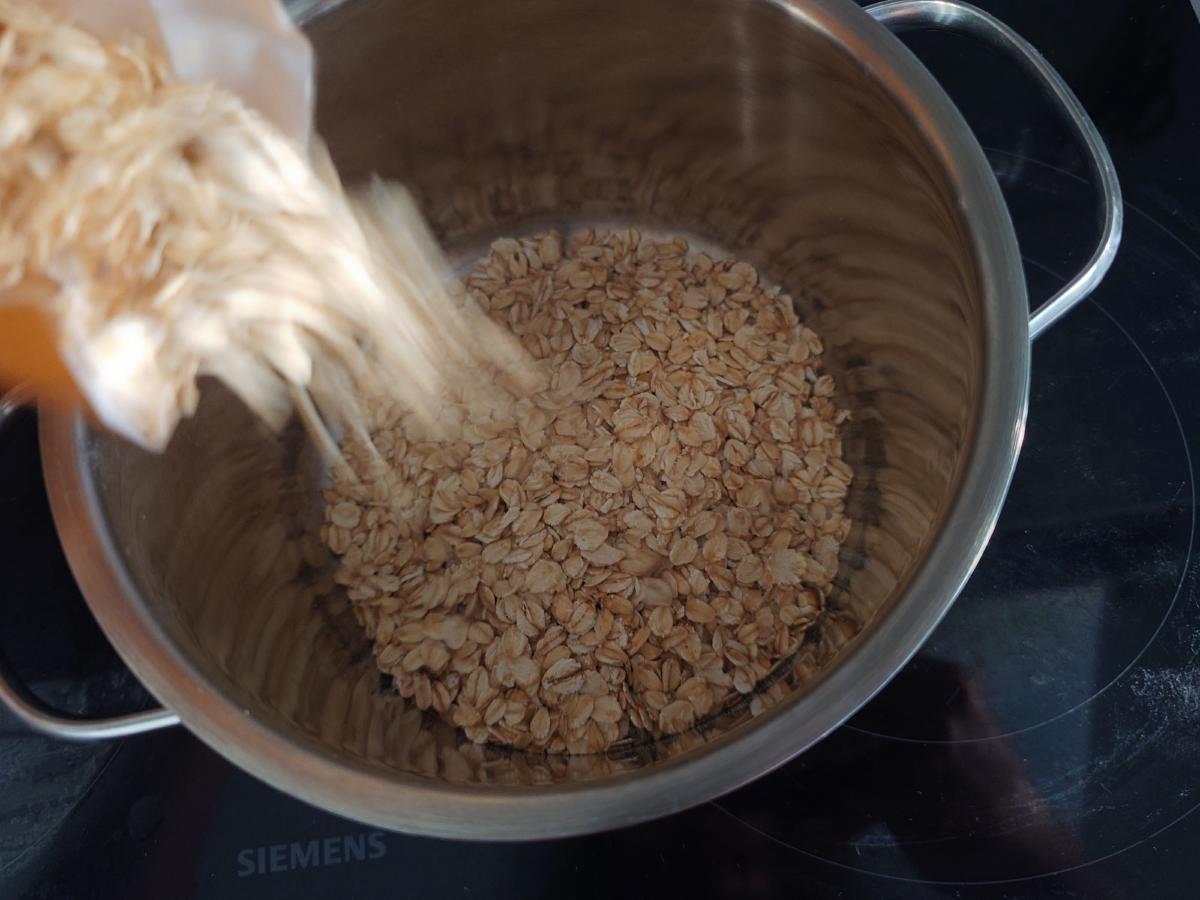 Rolled oats poured from the bag into a stainless pot on the hob