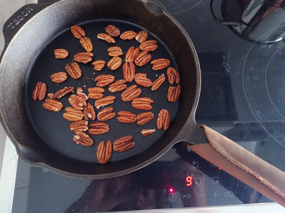 Raw pecan halves spread across a dry cast iron pan