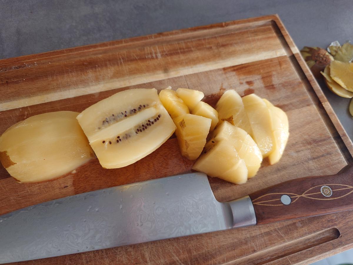 A peeled gold kiwi sliced and cut into chunks on the board