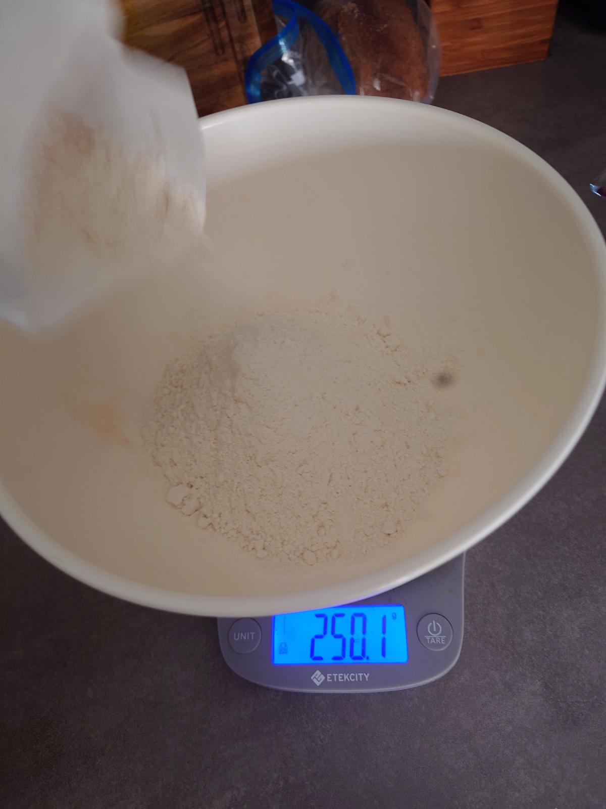Type 550 flour poured into the bowl, 250.1 g showing on the scale mid-pour