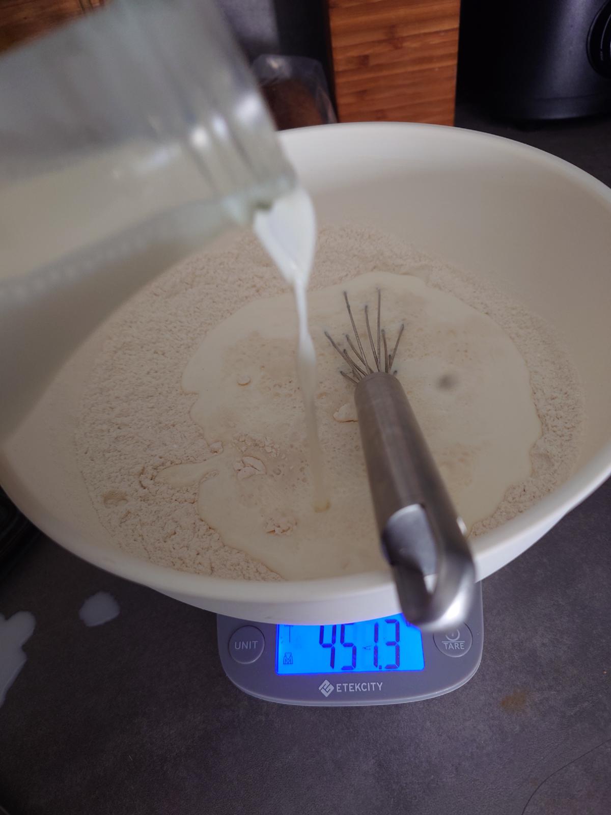 Milk poured from the jug into the flour, 451.3 g on the scale mid-pour