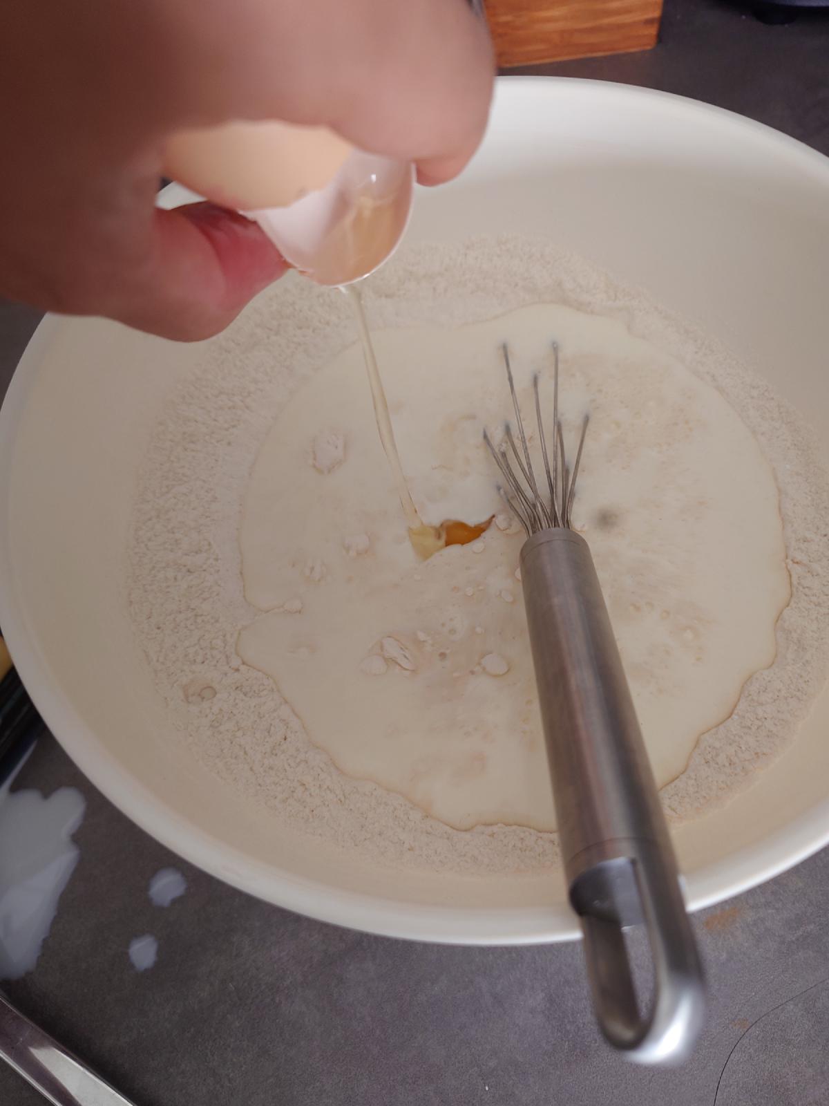 Egg cracked into the pool of milk in the middle of the flour