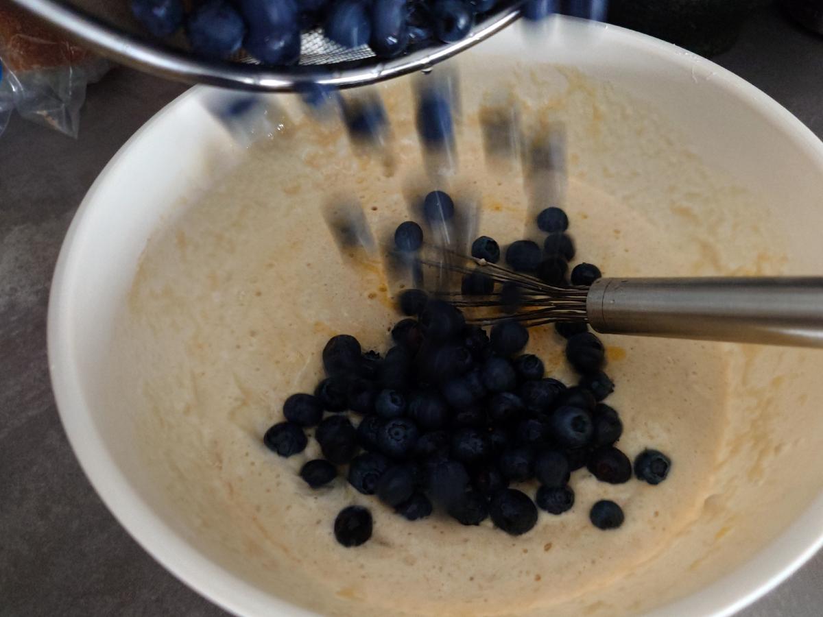 A colander of blueberries tipped into the mixed batter