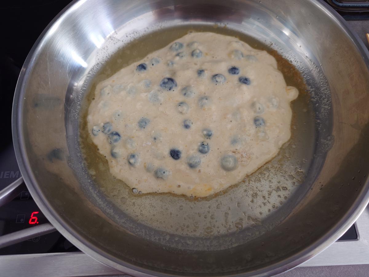 First pancake poured, blueberries showing through the batter