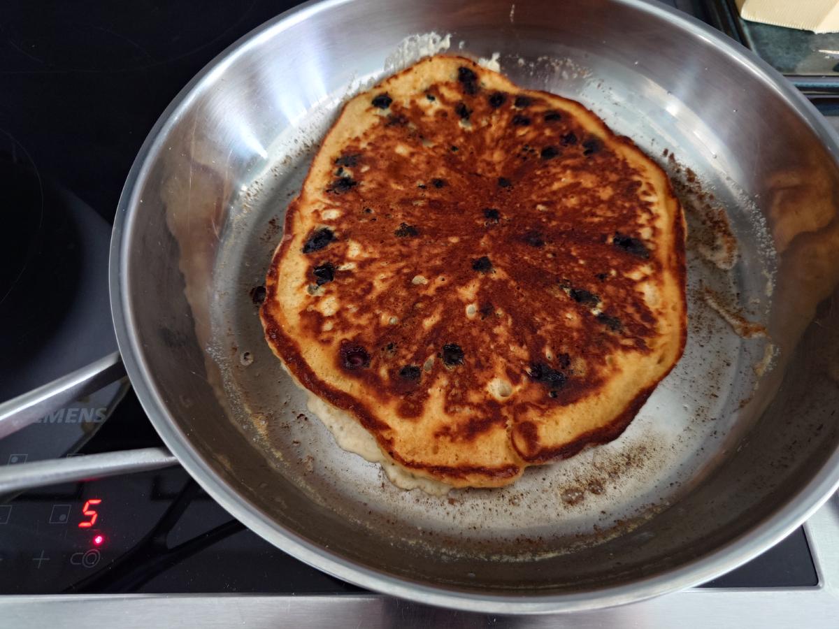 The first pancake flipped, the cooked side very dark brown with scorched blueberries