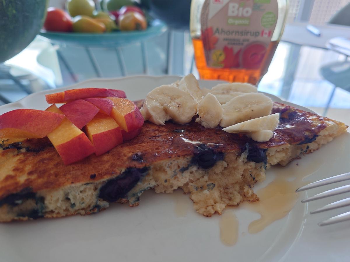 A pancake at the table with nectarine, banana and maple syrup, a bite cut out showing the crumb
