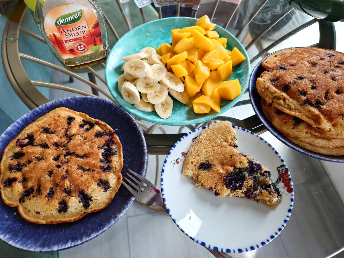 Breakfast table with blueberry pancakes, banana, mango and maple syrup