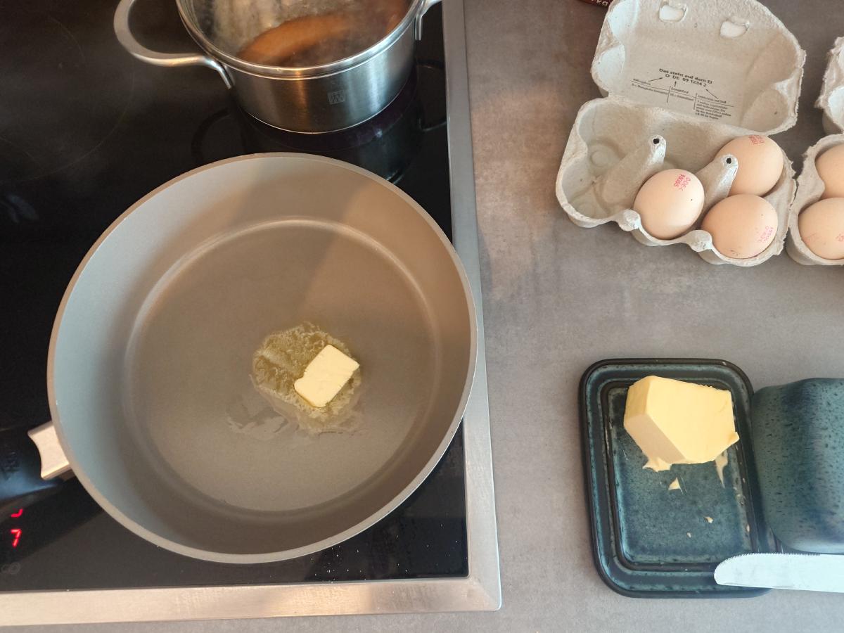 A knob of butter in a nonstick pan on the hob, eggs in the carton alongside