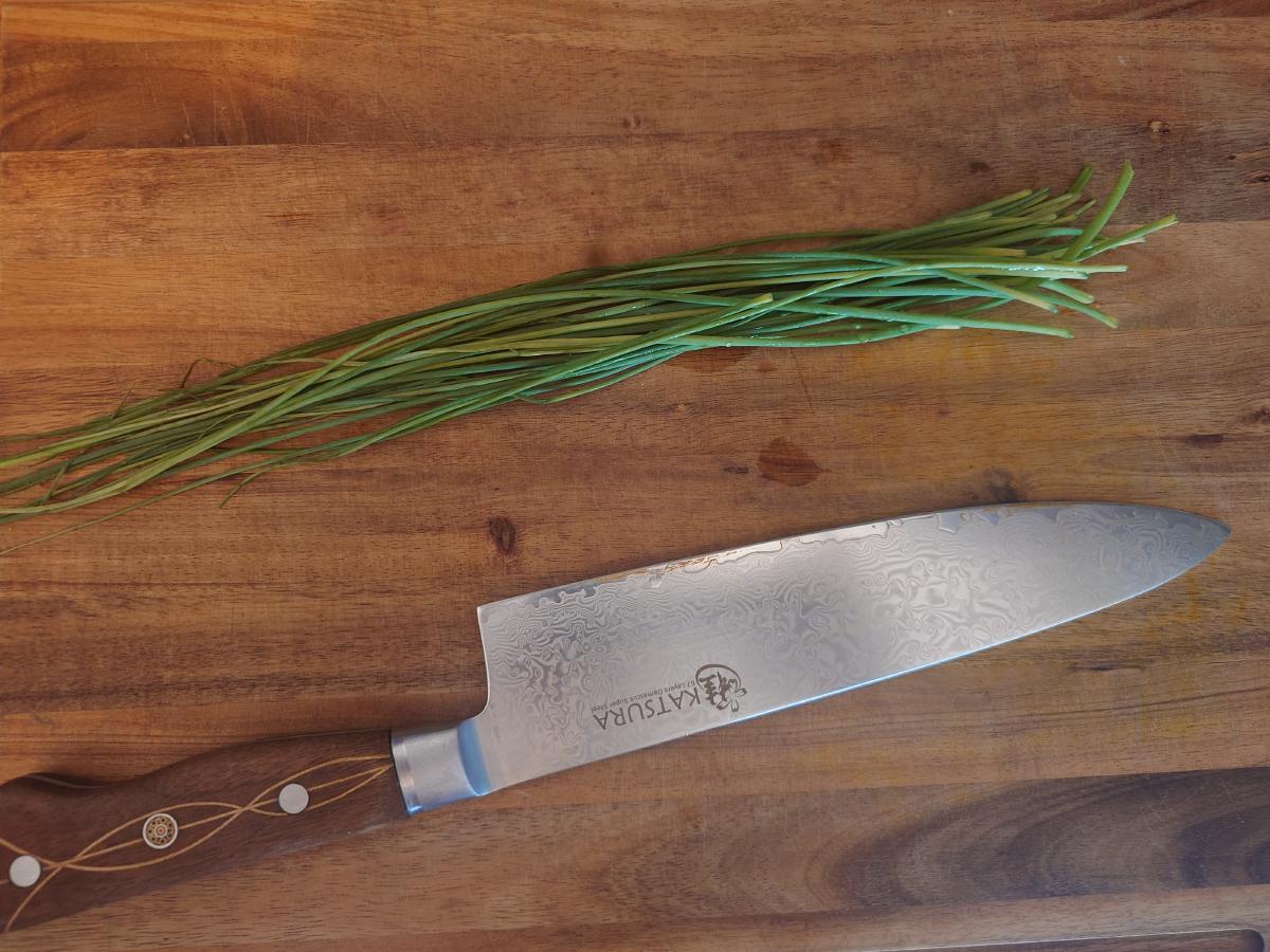 A bunch of chives on a wooden board next to a chef's knife
