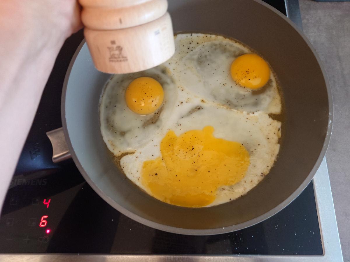 Three eggs cracked into the pan, salt and pepper being ground over them