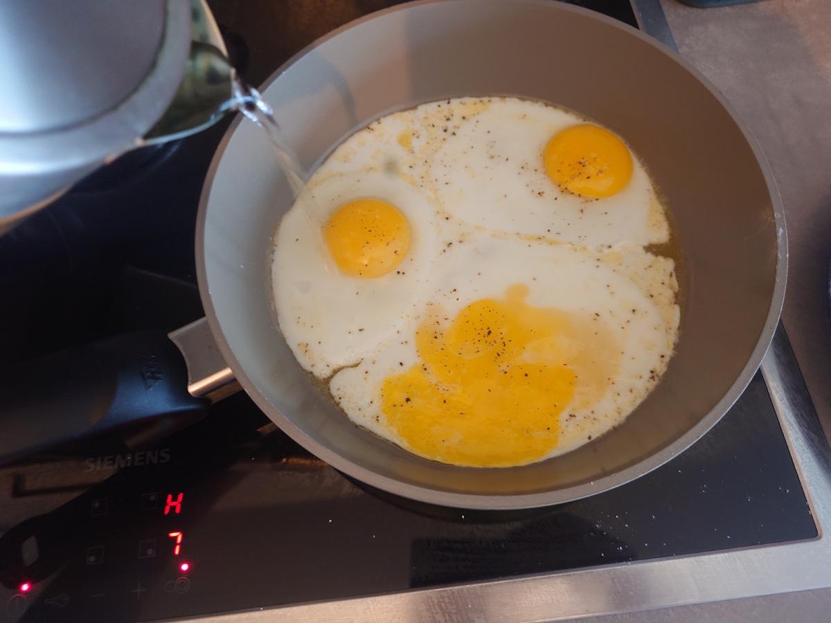 Water poured into the pan from a jug alongside the frying eggs