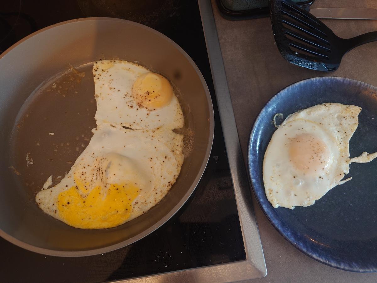 One egg lifted onto a blue plate, the other two still in the pan