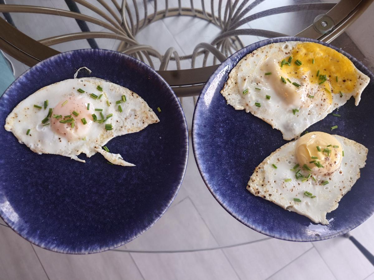 Two blue plates of fried eggs topped with chopped chives