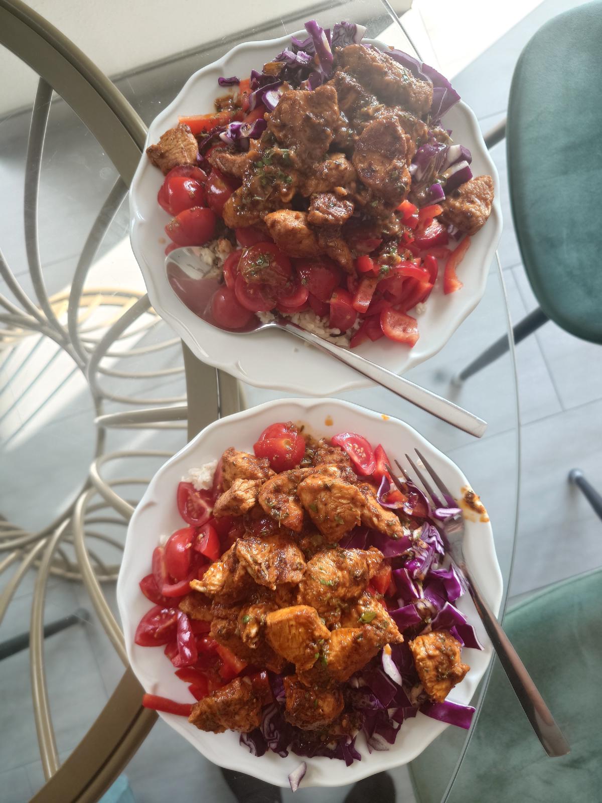 Two bowls of marinated chicken over rice with cherry tomatoes, red cabbage and pepper