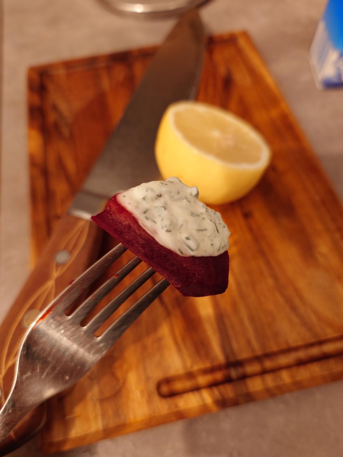 A beet baton on a fork with dill-chive yogurt spooned onto it